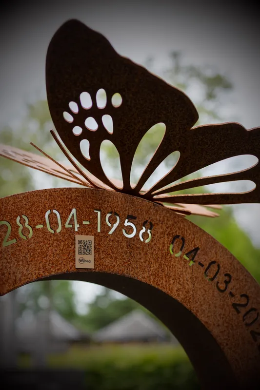 Wanagi QR-code geplaatst bij een cortenstaal monument met decoratieve halve boog en vlinder