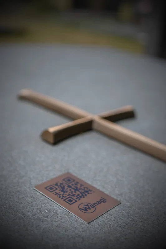Koperen Wanagi QR-code subtiel geplaatst onder een christelijk kruisje op een graf