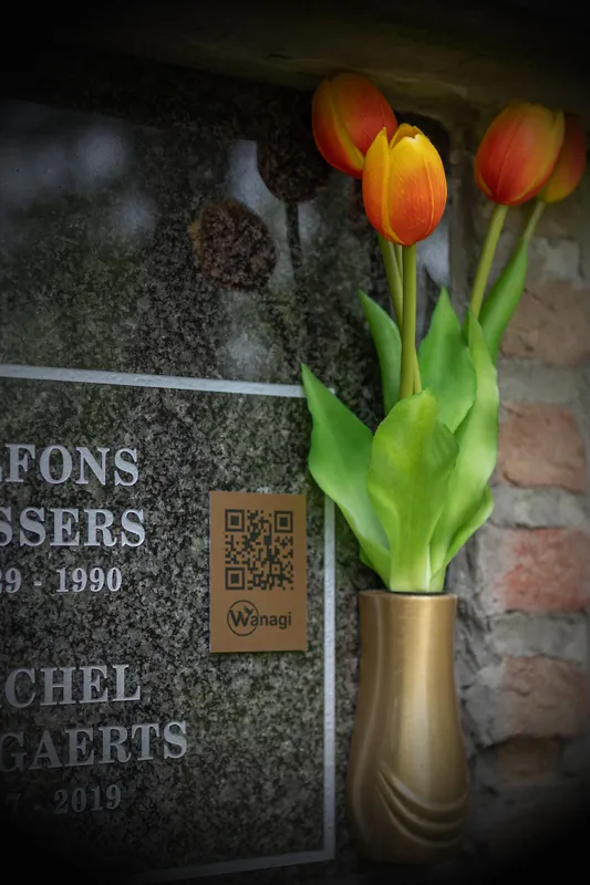 Wanagi QR-code plaatje gemonteerd op een donkere grafsteen naast een vaas met tulpen