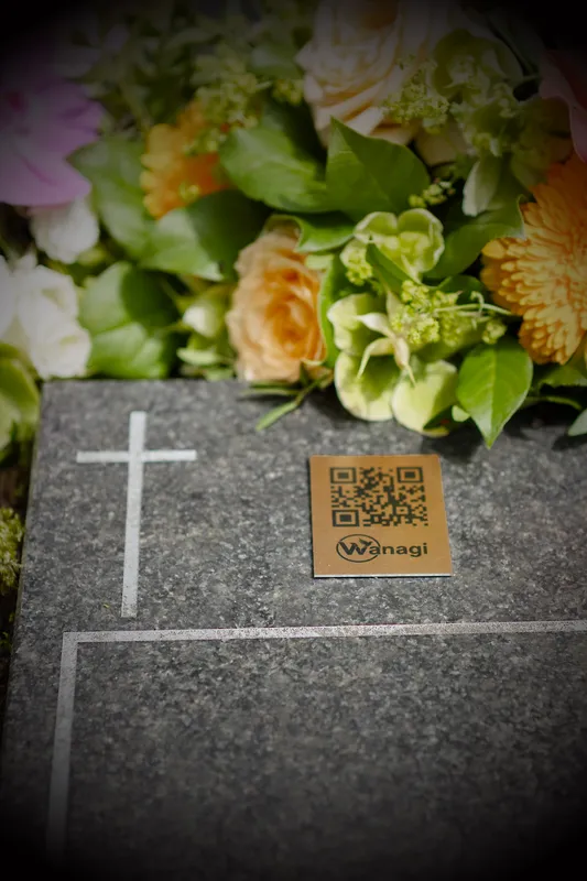 Wanagi QR-code plaatje respectvol bevestigd op een donkere granieten grafsteen naast verse bloemen