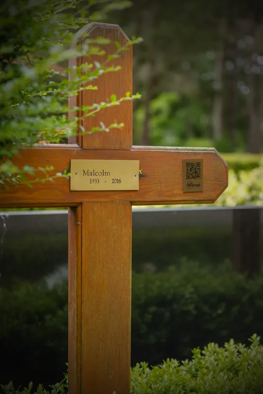 Wanagi QR gedenkplaatje bevestigd op een klassiek houten grafkruis op een grasveld