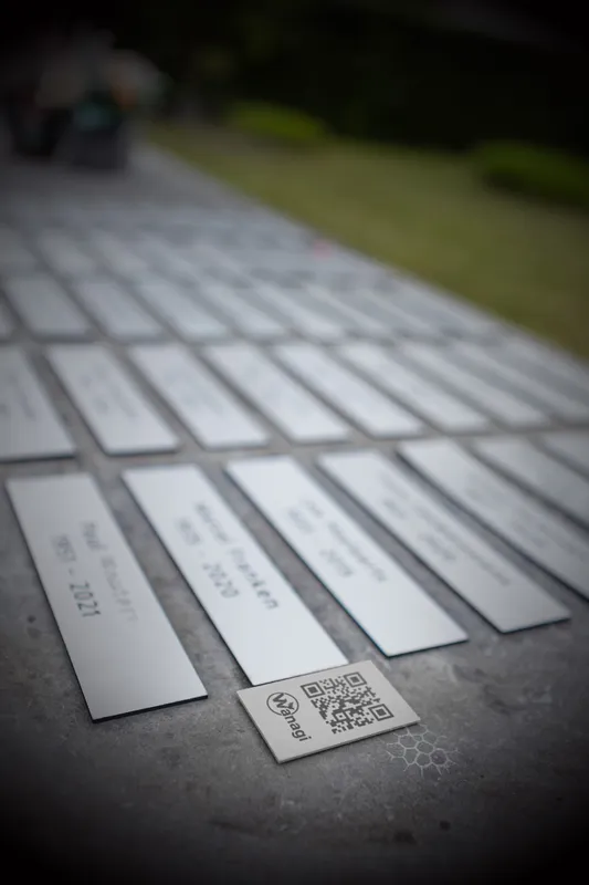 Metalen Wanagi QR-code blok geplaatst tussen gedenkplaten op een moderne begraafplaats