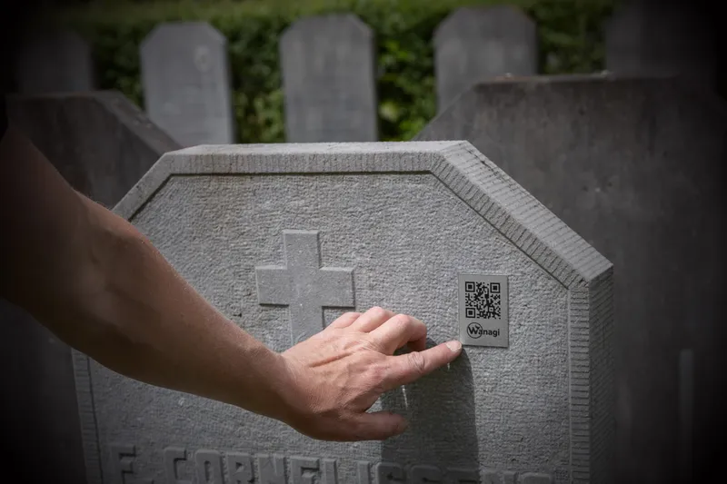 Hand die de Wanagi QR-code aanwijst om te scannen op een lichte, grijze gedenksteen